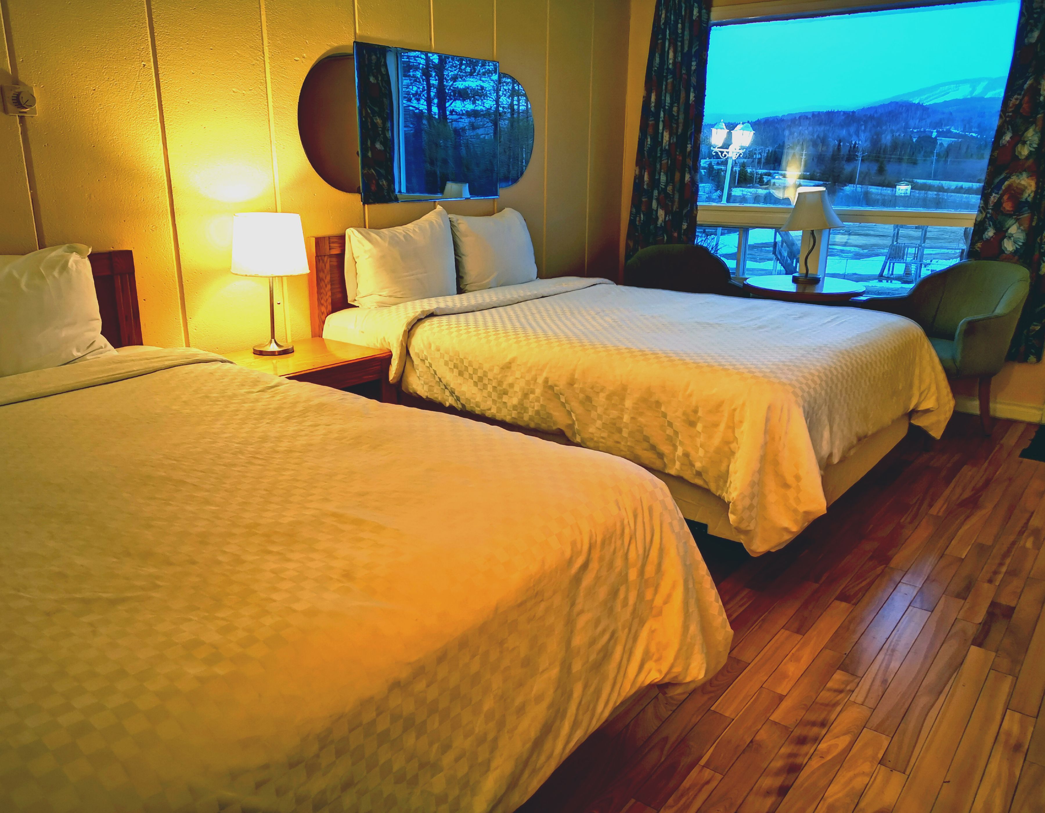 A hotel room with two beds, a TV mounted on the wall, and a view of a snowy landscape through the window.