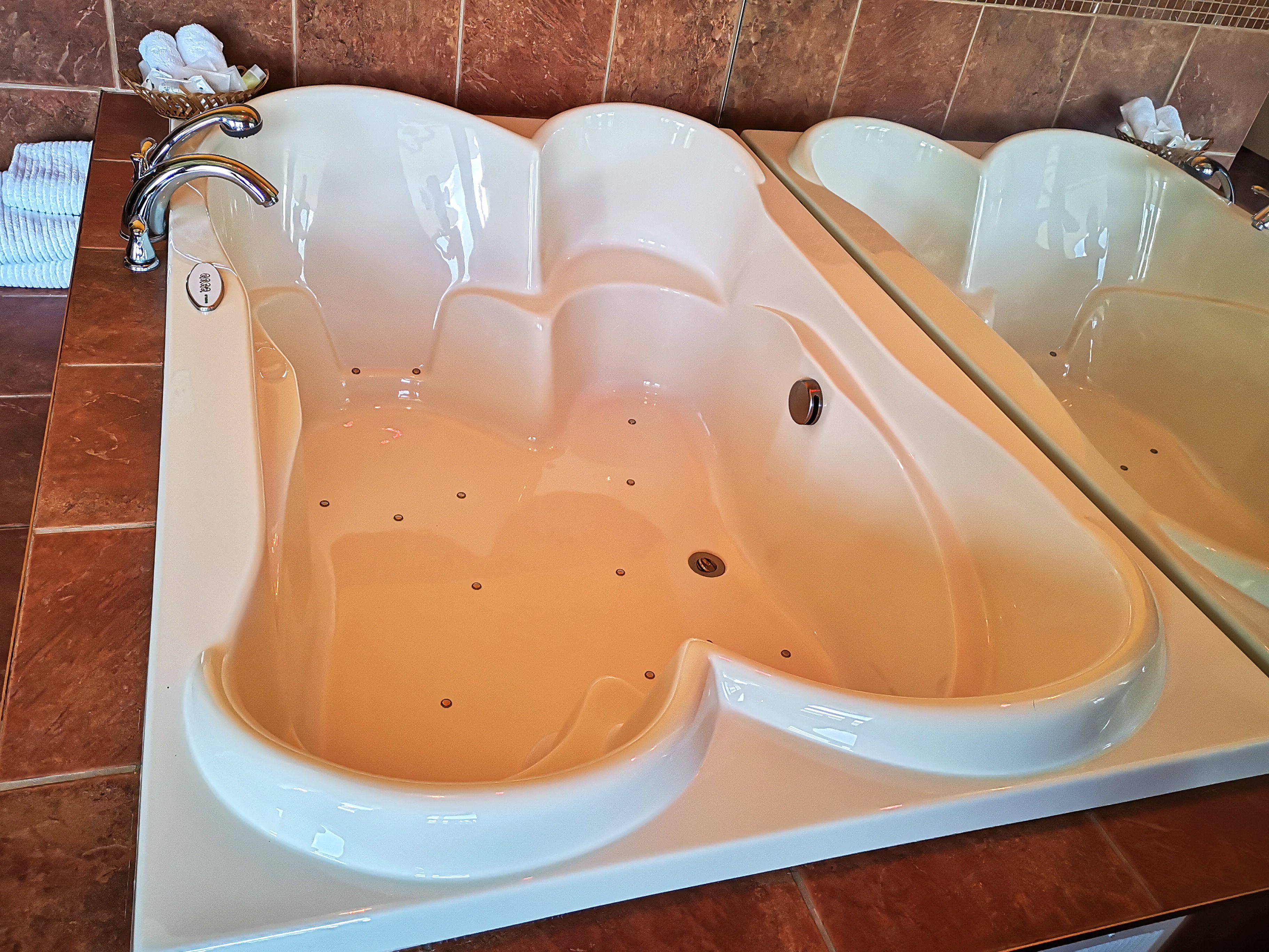 A large, white, freestanding bathtub with a single faucet and control knob, set against a tiled wall.