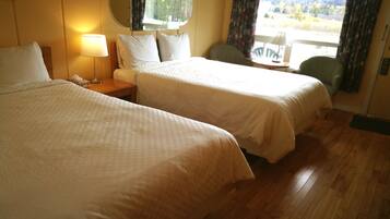 A hotel room with two beds, a nightstand with a lamp, a chair, and a view of the outdoors.