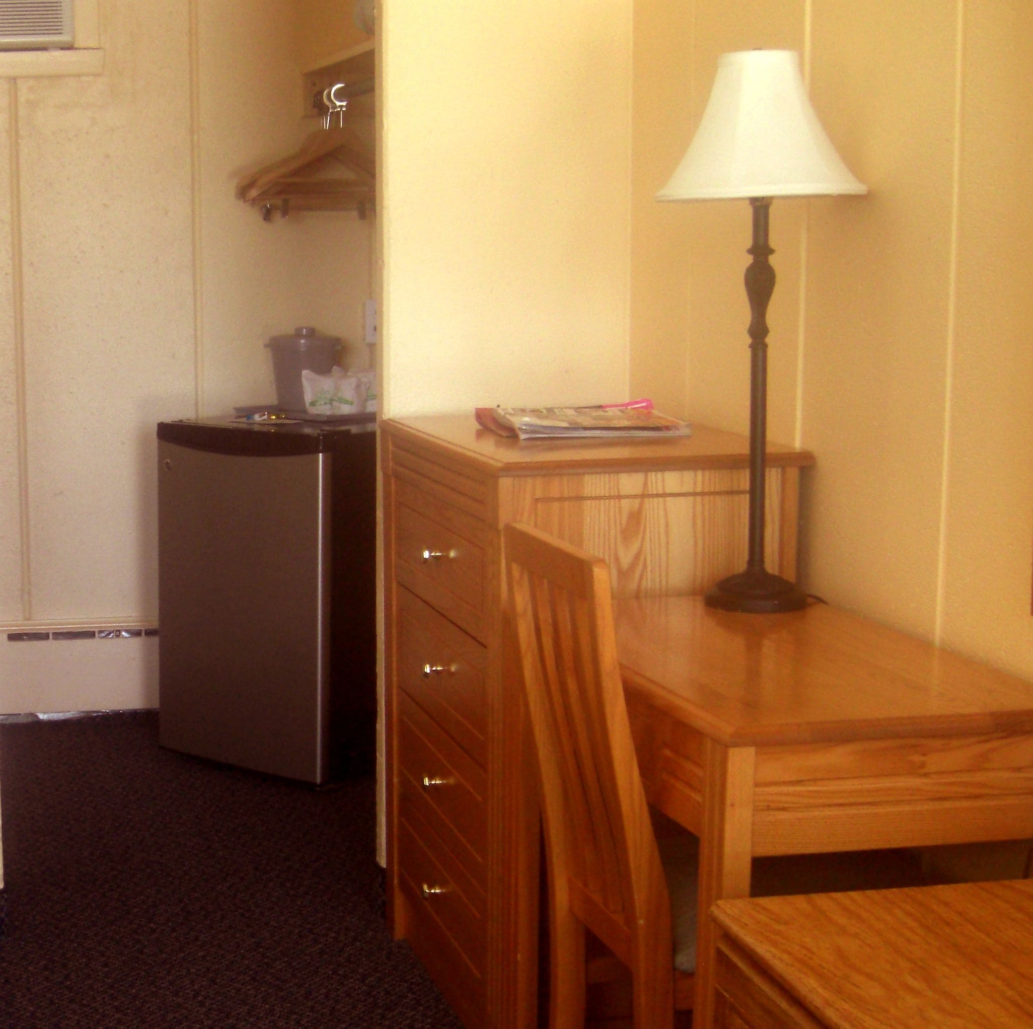 Una kitchenette compacta con refrigerador, una mesa de madera y una lámpara.