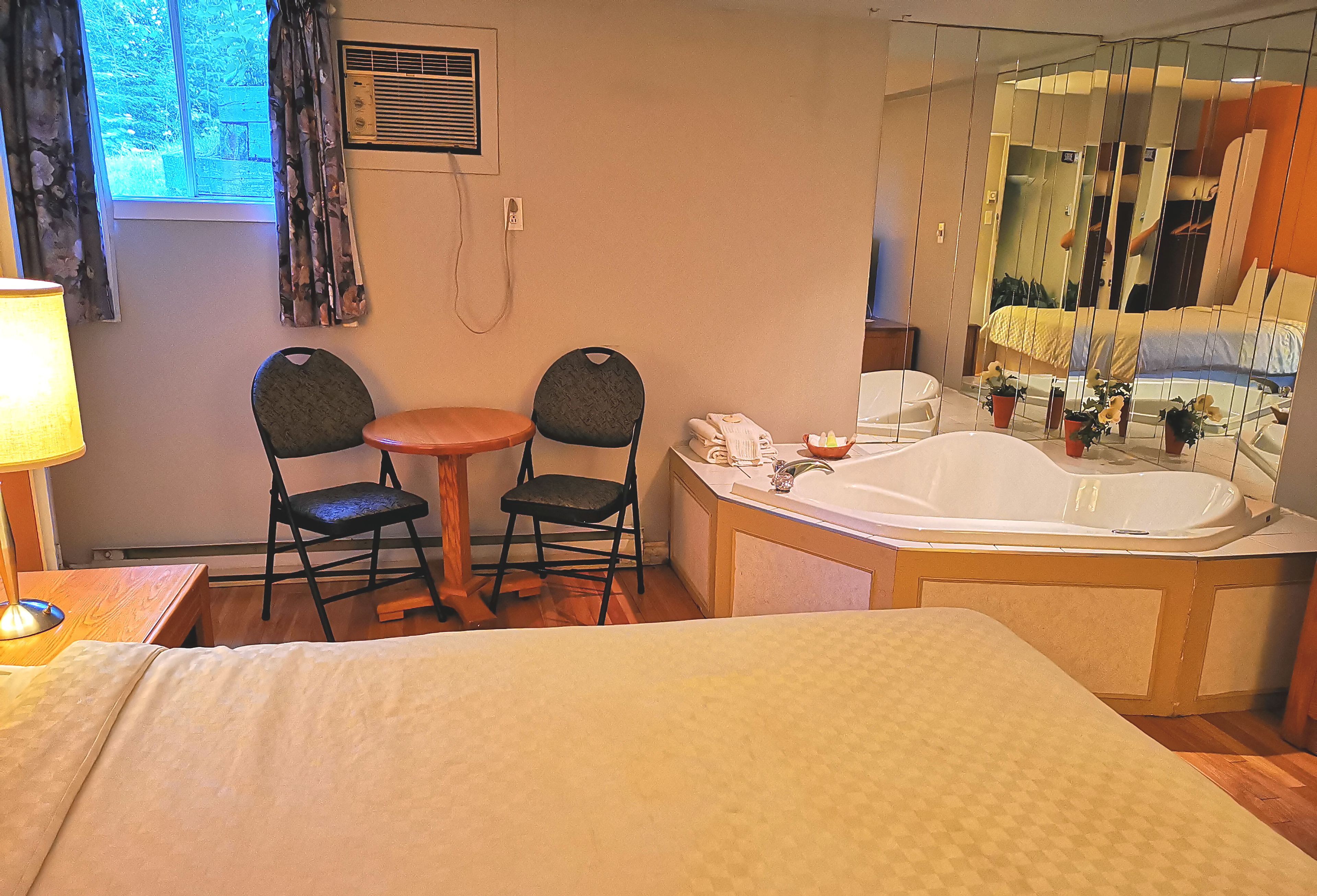 A hotel room with a bed, a small table with two chairs, a bathroom with a bathtub, and a large mirror.