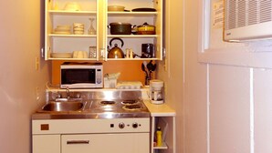 A compact kitchen with a microwave, stove, and open shelves containing dishes and cookware. - Motel Tremblant (Mont-Blanc)