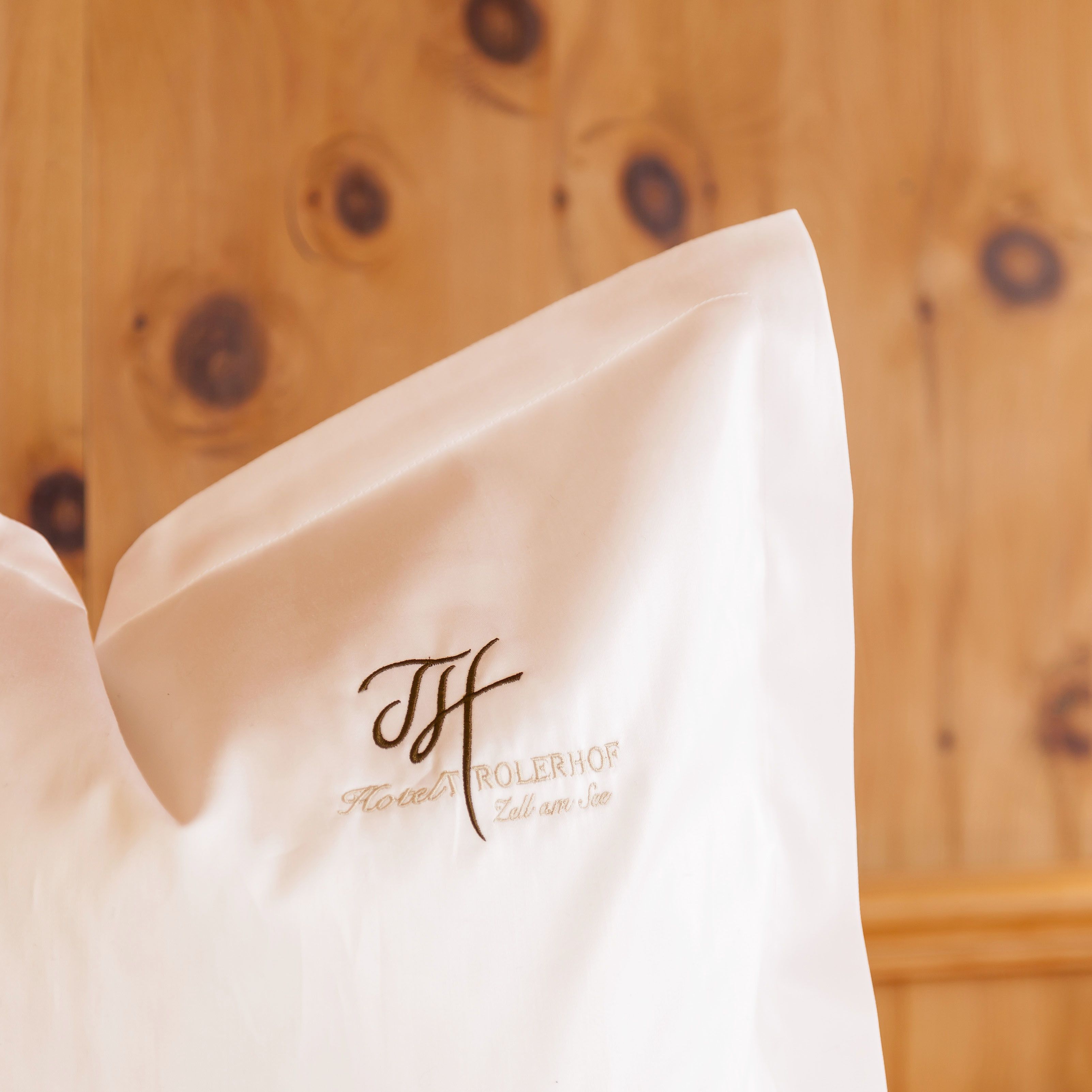 A white pillow with embroidered text and logo, against a wooden background.