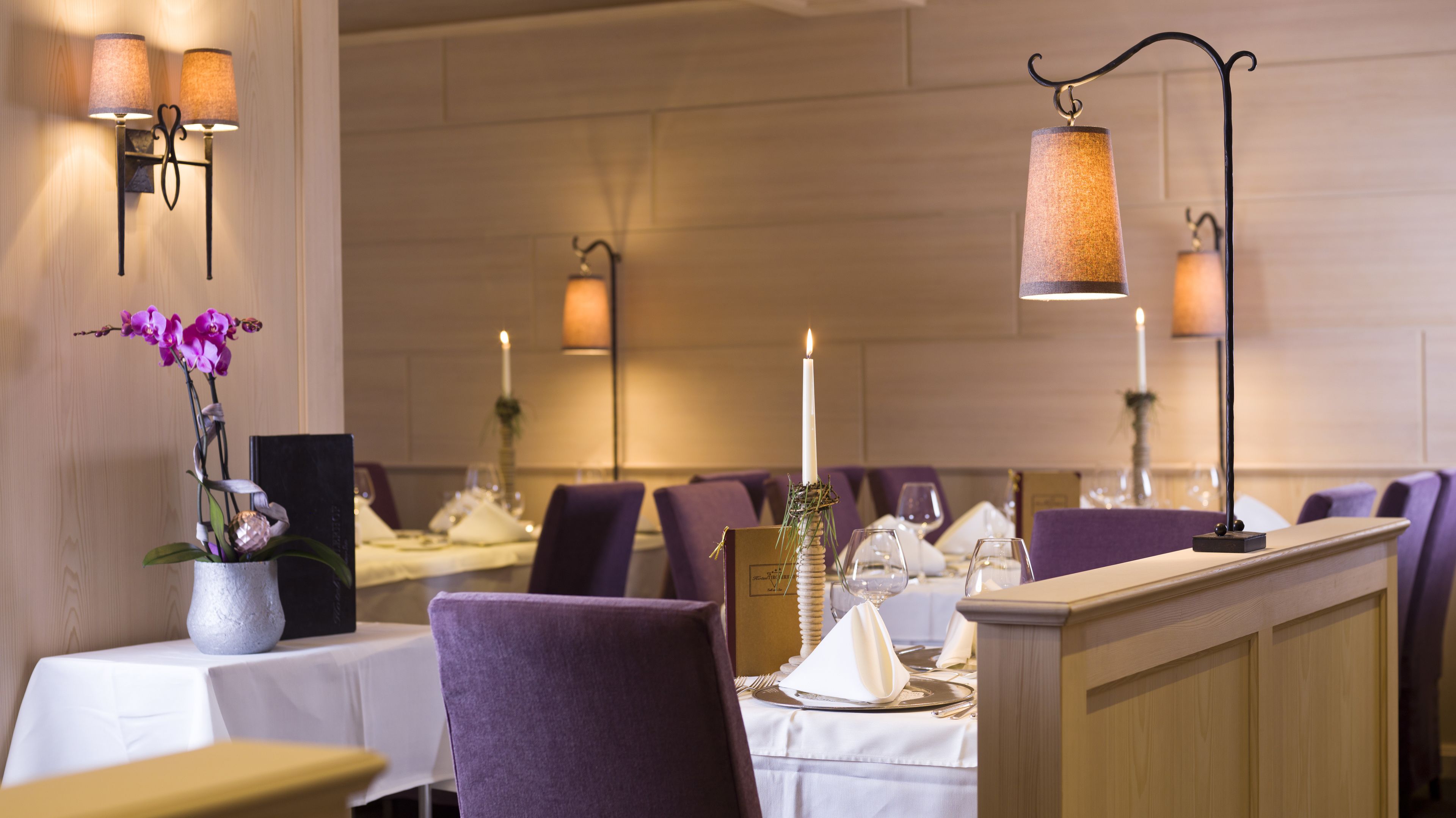 Un restaurante con sillas moradas, manteles blancos y mesas iluminadas con velas.