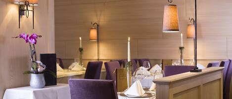 En restaurant med lilla stole, hvide duge og borde med levende lys.