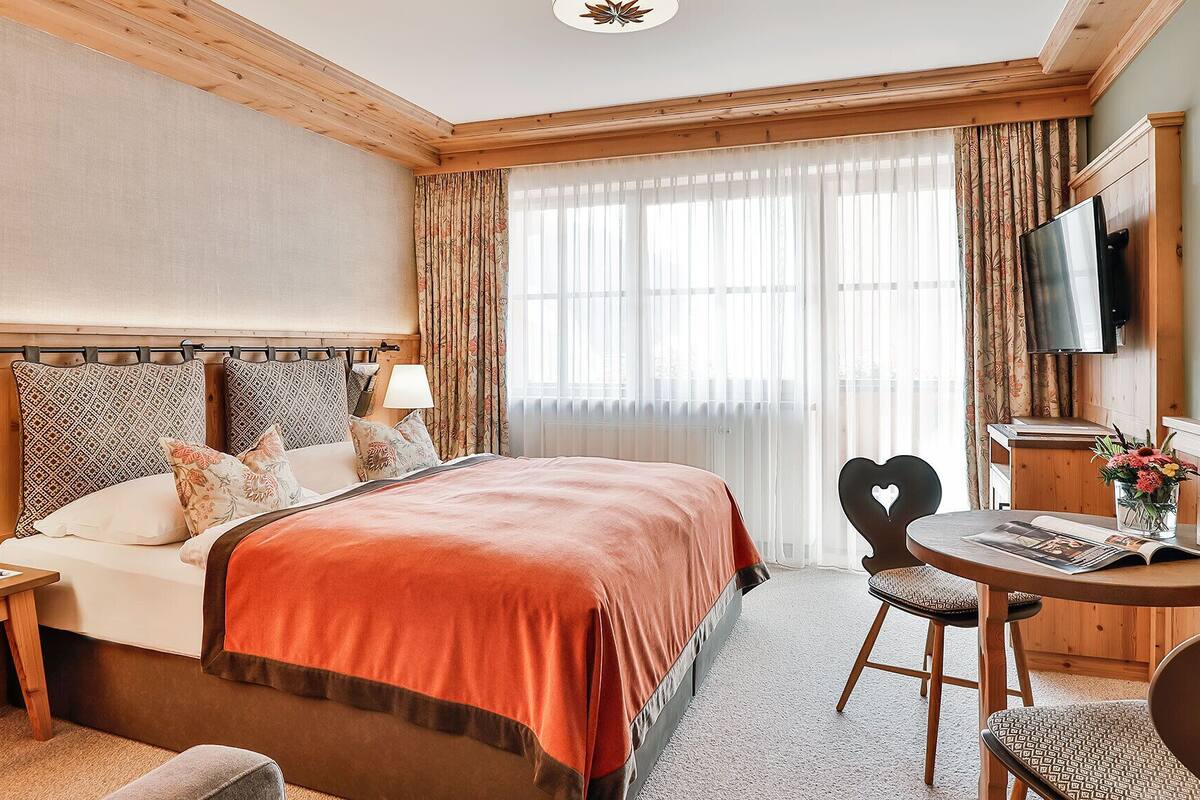 A hotel room with a large bed, a desk with a chair, a television, and a window with curtains.