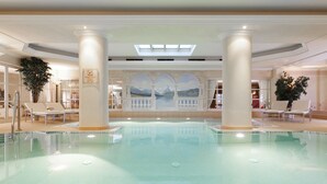 Una amplia piscina cubierta con un mural de montañas y un lago, rodeada de columnas y sillones de descanso.