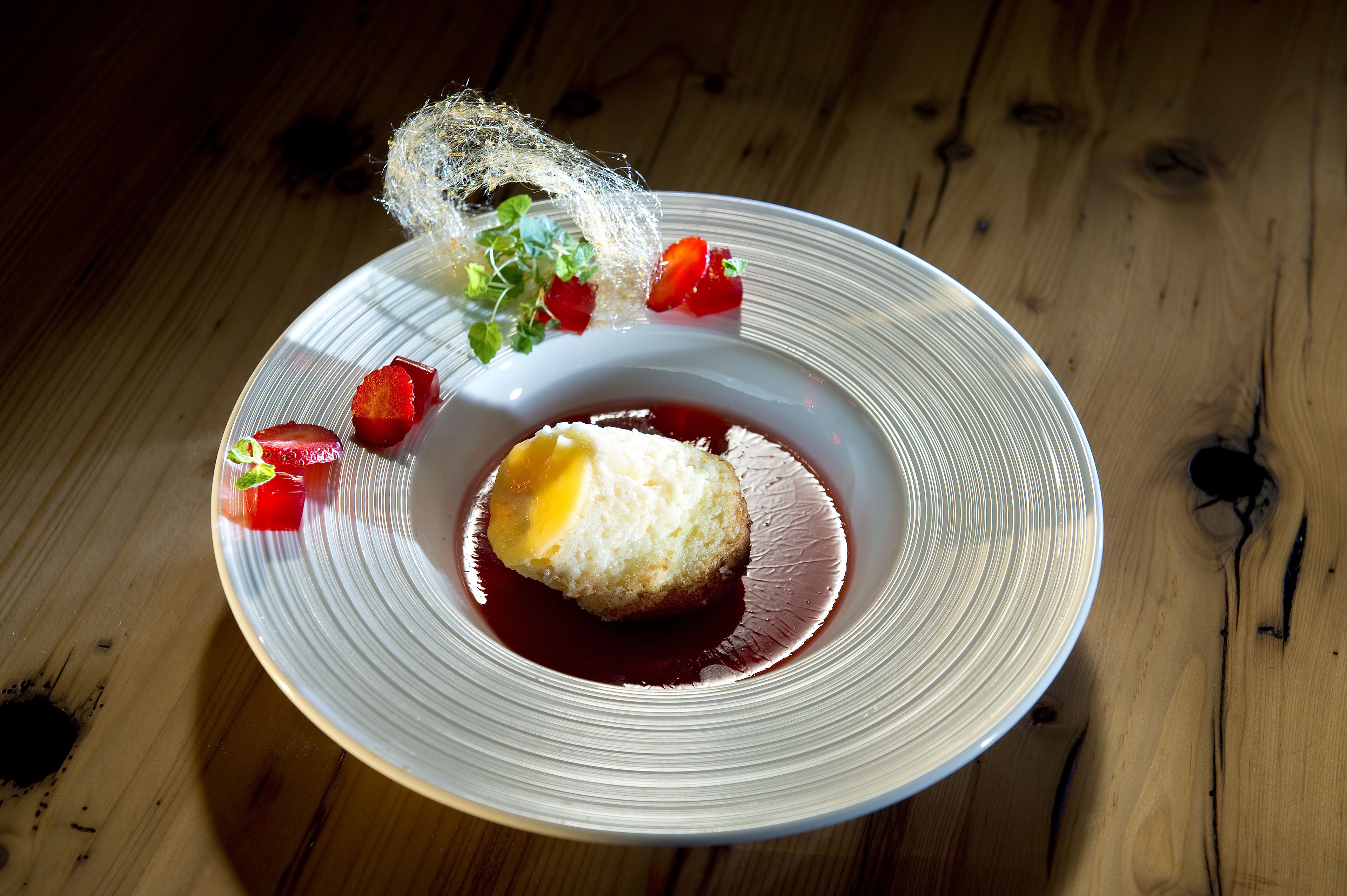A dessert on a white plate with strawberries and a decorative element on a wooden table.