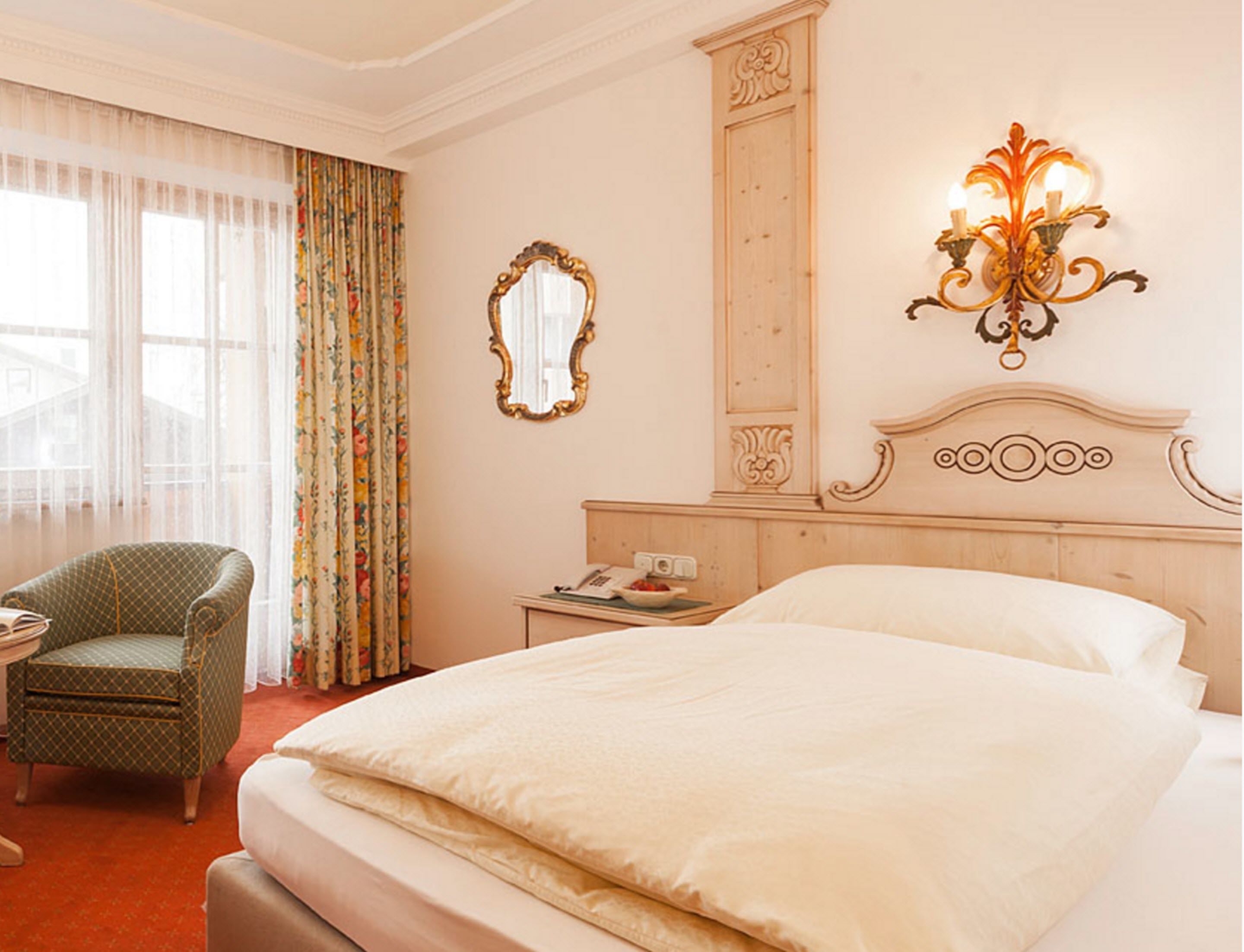 Habitación de hotel con una cama grande, una silla, una mesita de noche, un espejo y una lámpara fijada a la pared.