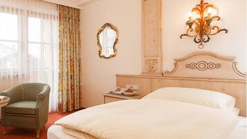 Habitación de hotel con una cama grande, una silla, una mesita de noche, un espejo y una lámpara fijada a la pared.