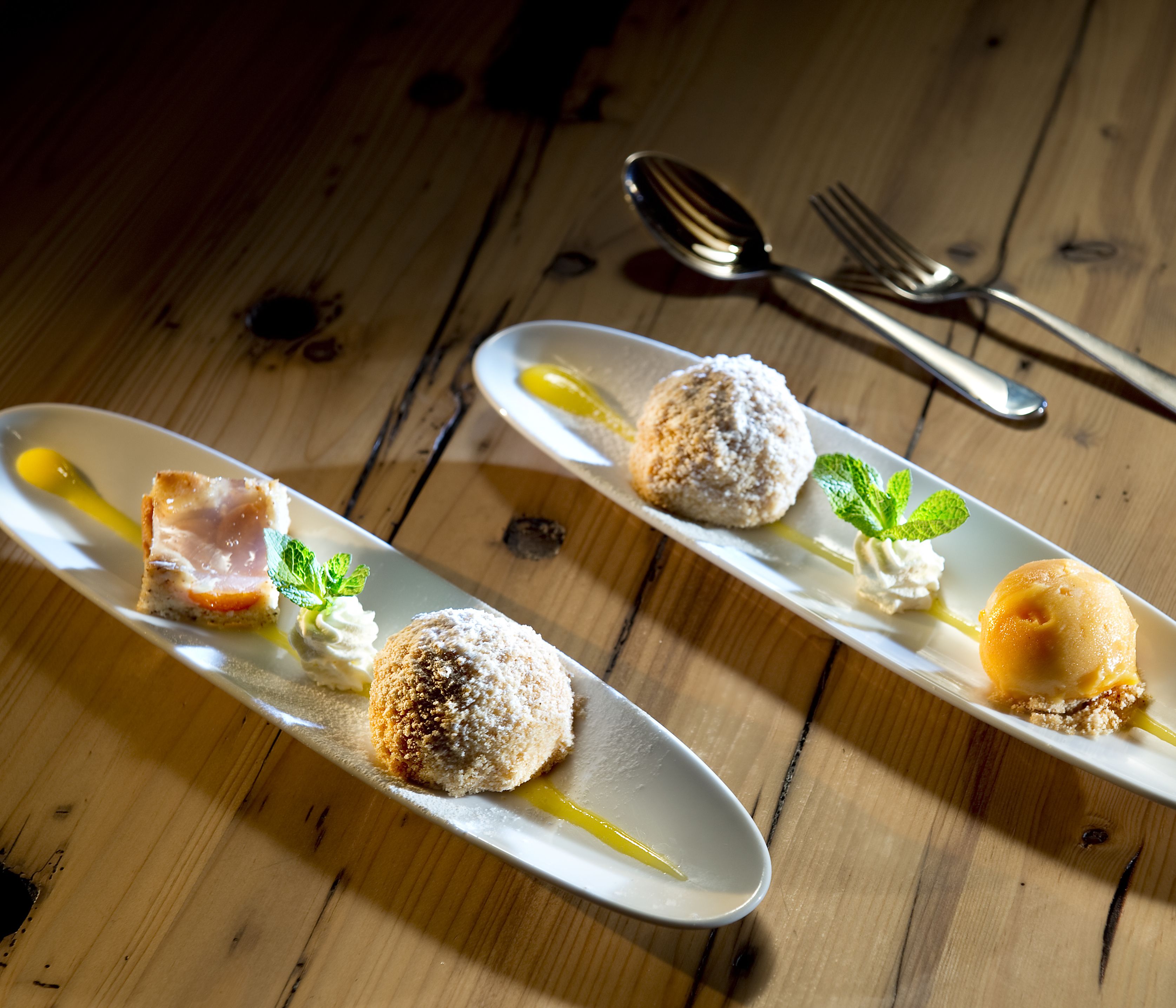 Two plated desserts on a wooden table with a fork and spoon.