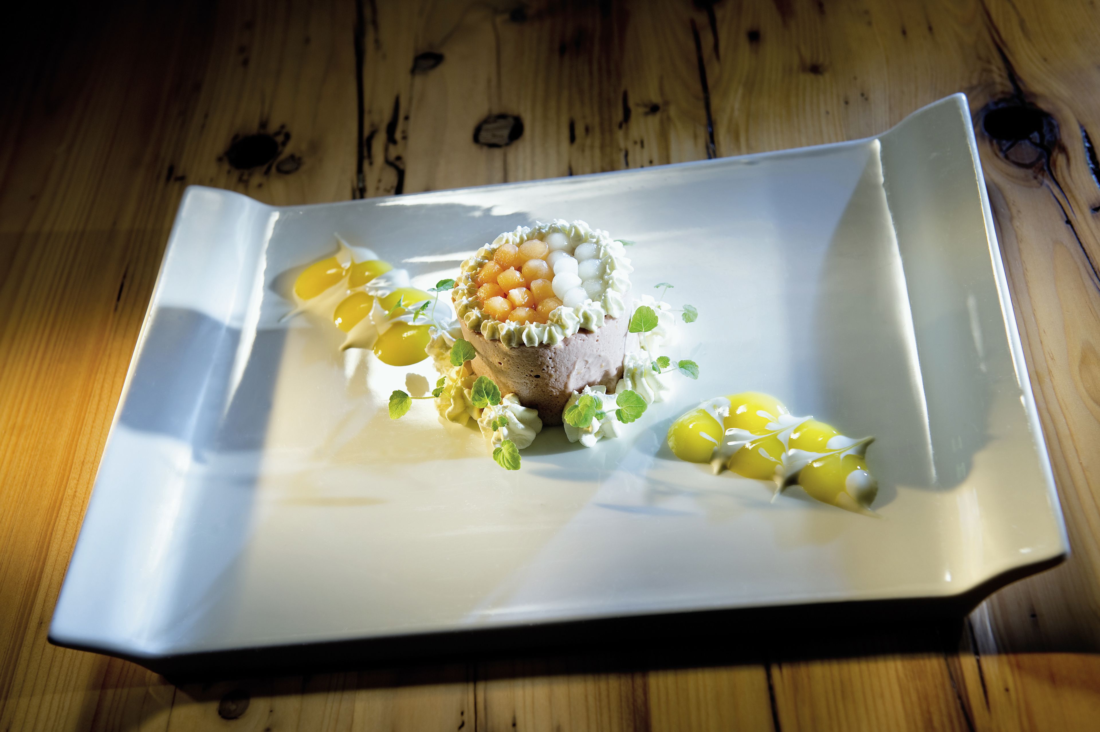 A square plate with a dish of meat, caviar, and garnishes on a wooden table.