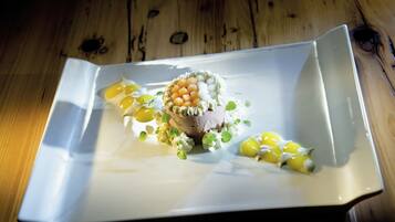 Un plato cuadrado con un guiso de carne, caviar y adornos sobre una mesa de madera.