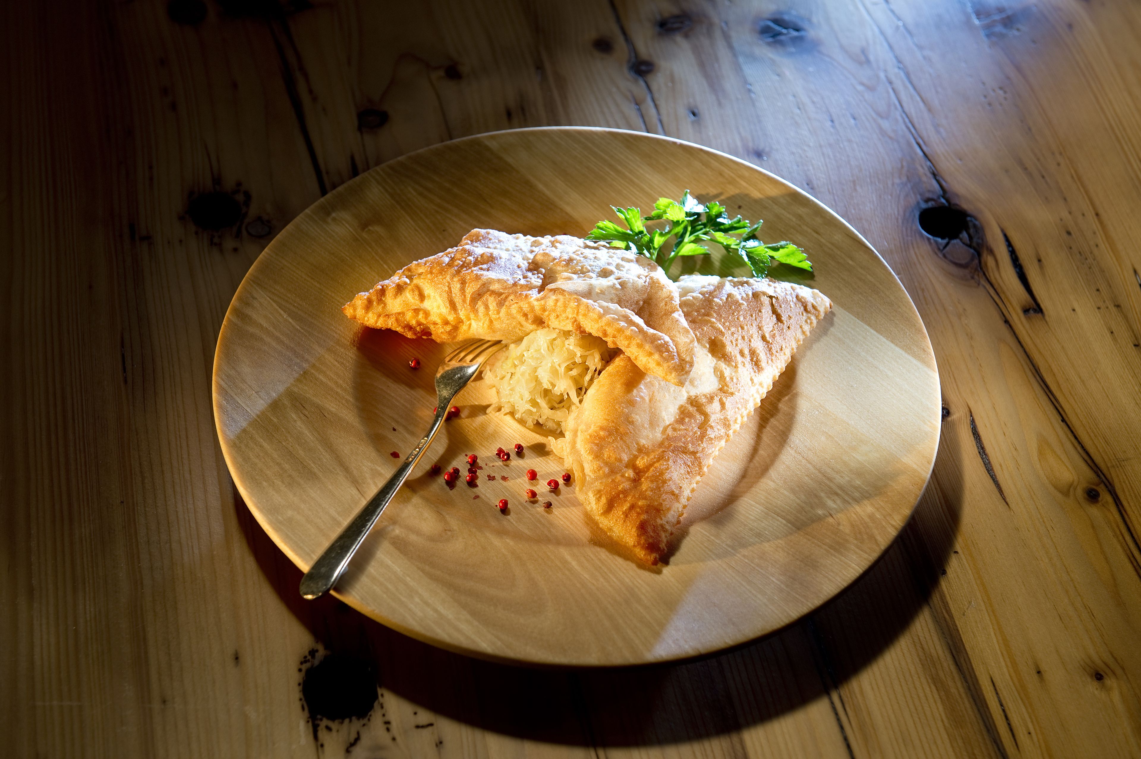 A wooden table with a round plate containing a folded pastry and a fork.