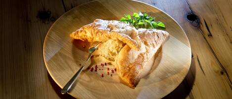 A wooden table with a round plate containing a folded pastry and a fork.