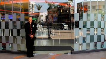 A man in uniform standing in front of a modern building with reflective glass panels and palm tree motifs.
