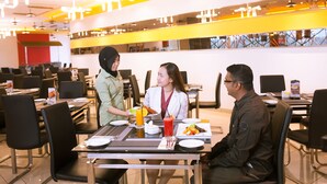 A modern dining area with multiple tables and chairs, a bright yellow accent wall, and a view of the cityscape through large windows. - Palm Seremban Hotel (Seremban)