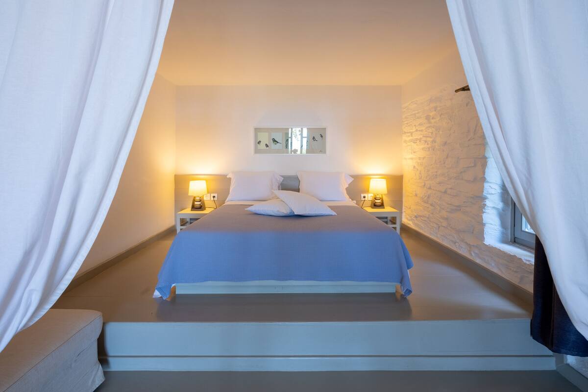 Ein Schlafzimmer mit einem Bett, zwei Nachttischen mit Lampen, einem Wandbild und einer Steinwand.