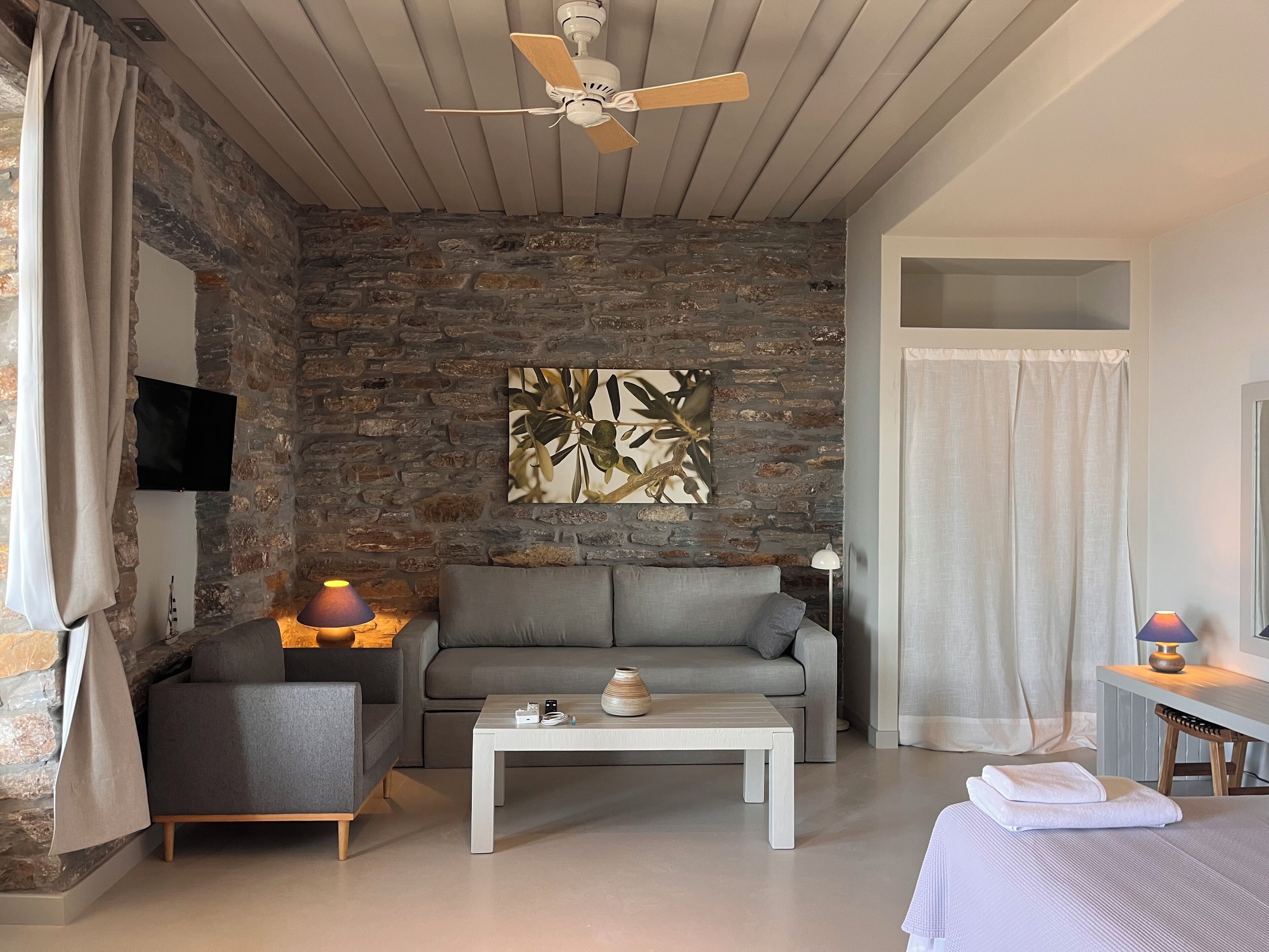 A modern living room with a stone wall, a grey sofa, a coffee table, and a ceiling fan.