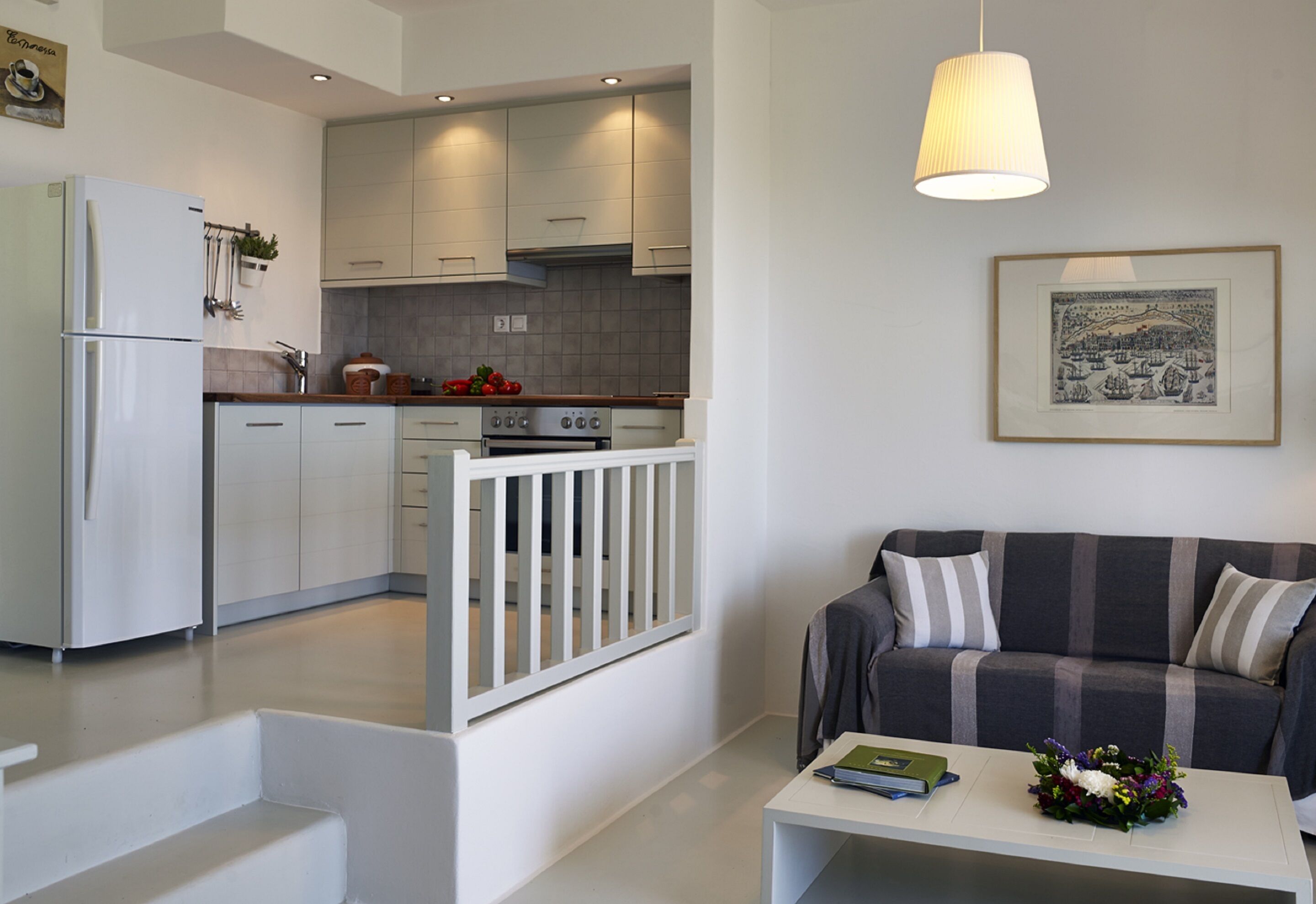 A modern kitchen with white cabinets, a built-in oven, and a dining area with a white table and a striped sofa.