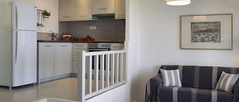 A modern kitchen with white cabinets, a built-in oven, and a dining area with a white table and a striped sofa.