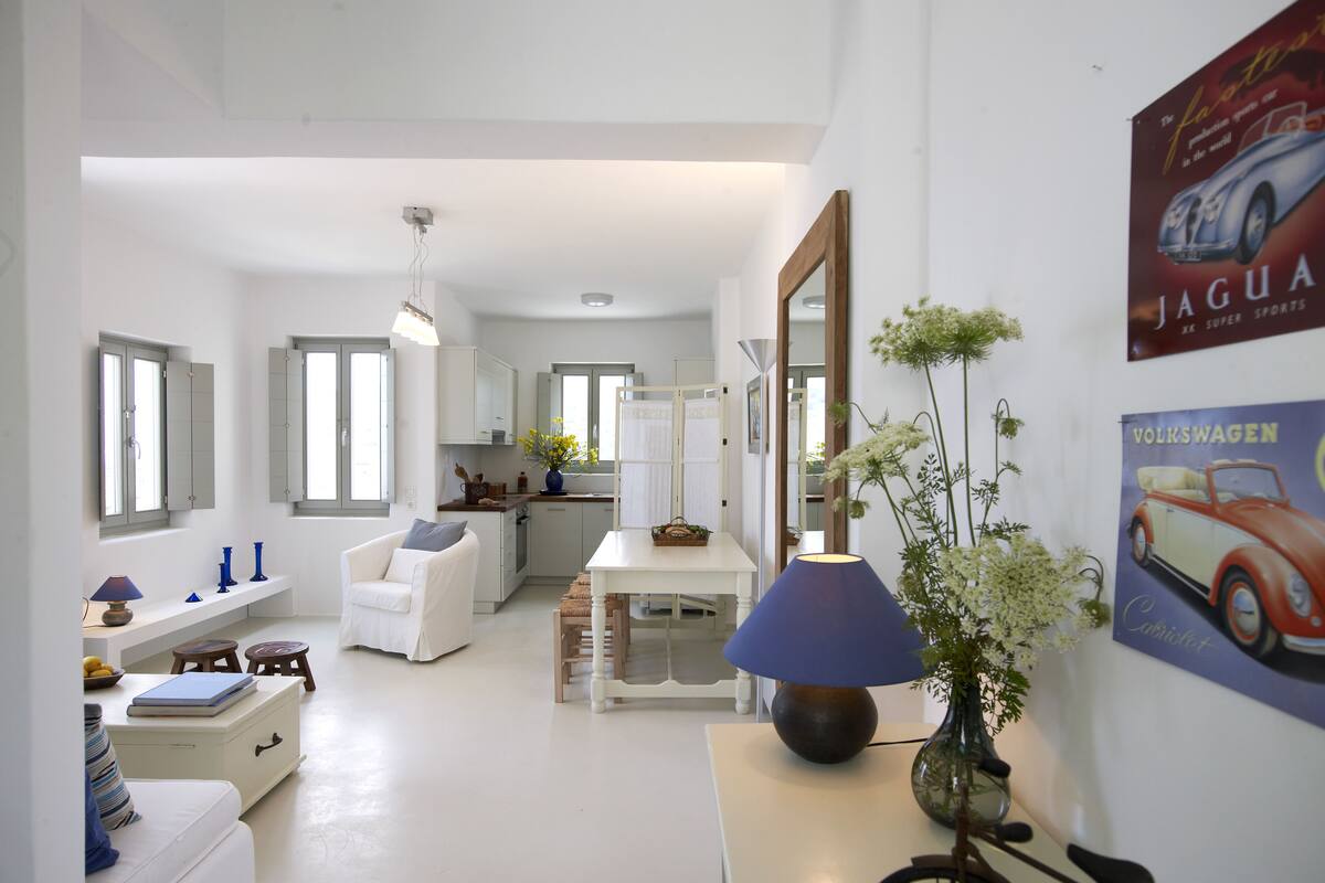 Ein modernes, helles Wohnzimmer mit einer Couch, einem Esstisch und einer Küche im Hintergrund.
