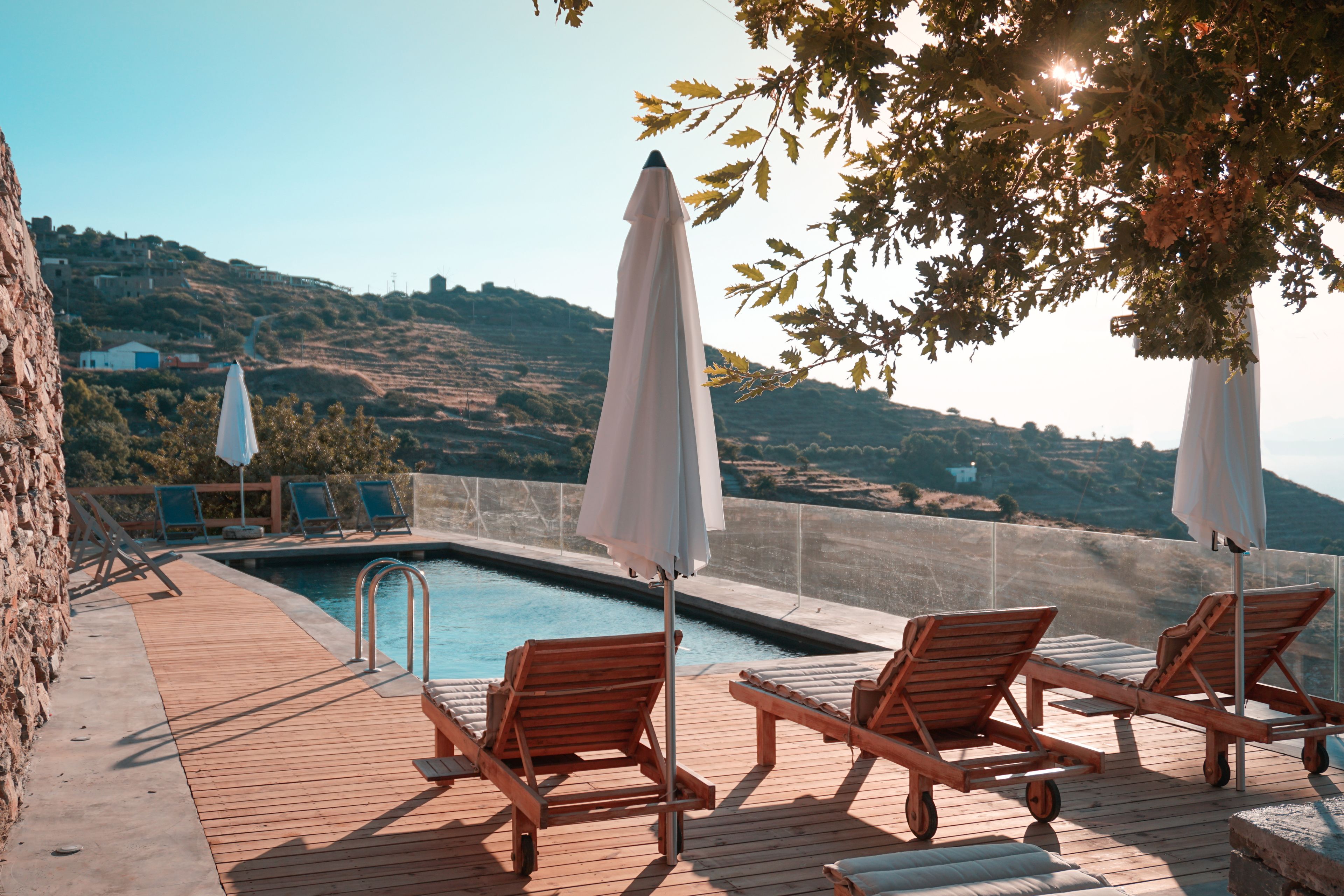 Eine Holzterrasse mit Liegestühlen und Sonnenschirmen mit Blick auf einen Pool, mit Hügeln im Hintergrund.