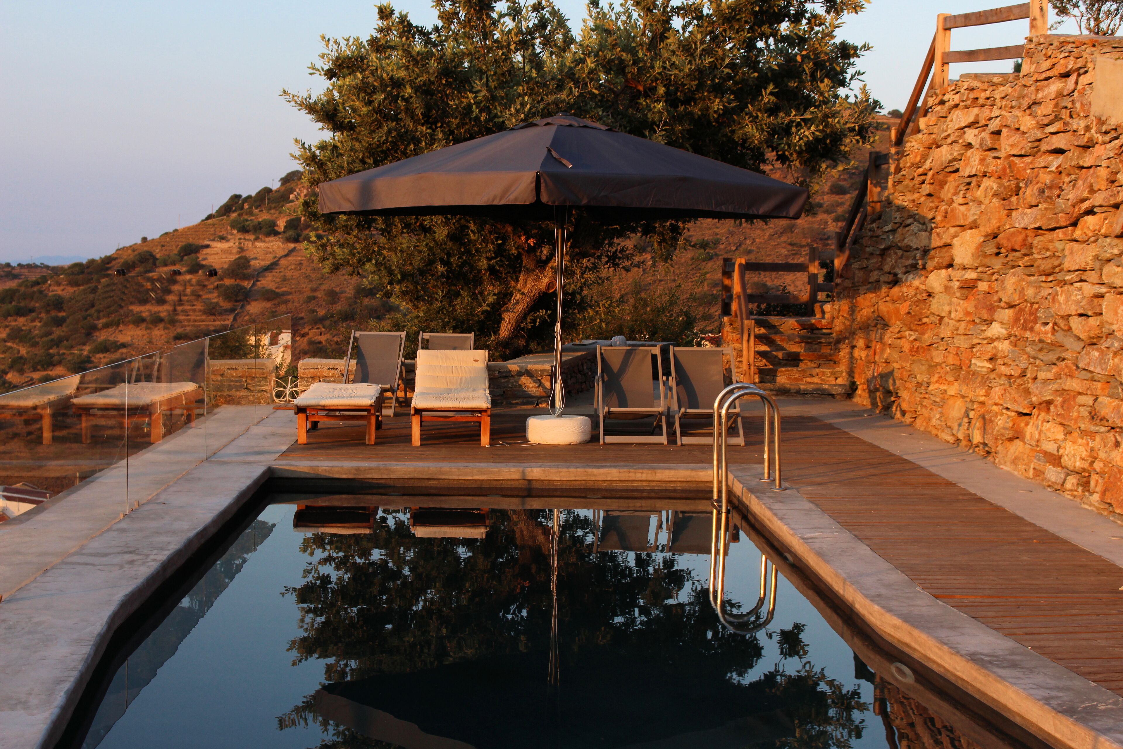 A poolside area with lounge chairs, a wooden deck, and a stone wall.