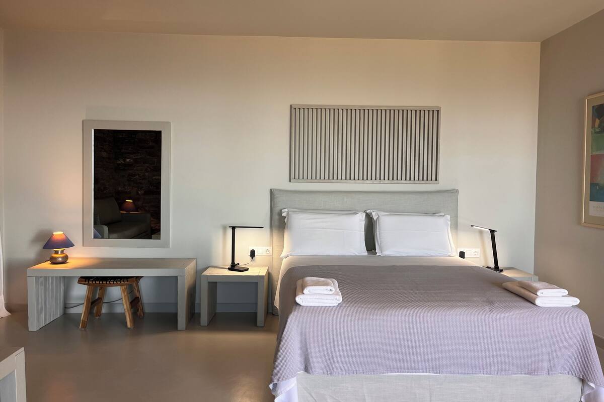 Ein modernes Hotelzimmer mit Bett, Nachttischen, einem Schreibtisch und einem Sessel.