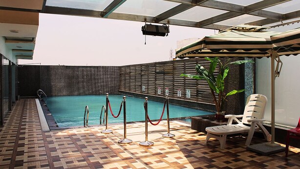 An indoor swimming pool with a tiled floor, a glass ceiling, and a poolside area with a chair and a potted plant. - Hotel Chennai Le Palace (Chennai)