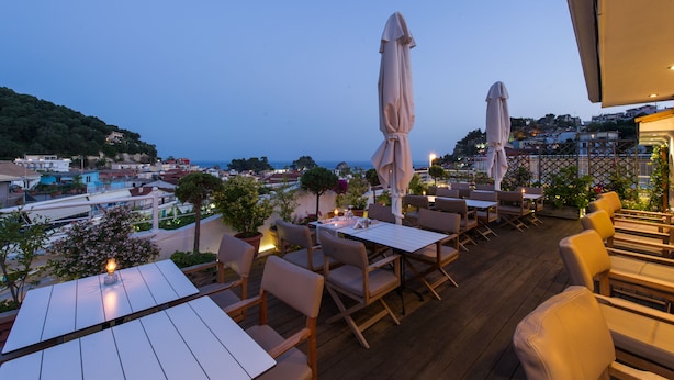 An outdoor dining area with tables and chairs, umbrellas, and potted plants. - Olympic Hotel (Parga)