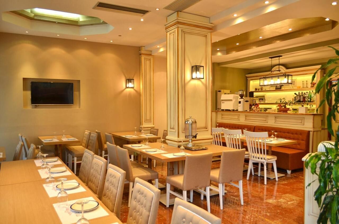 A hotel dining area with multiple tables and chairs, a bar, and a television screen.