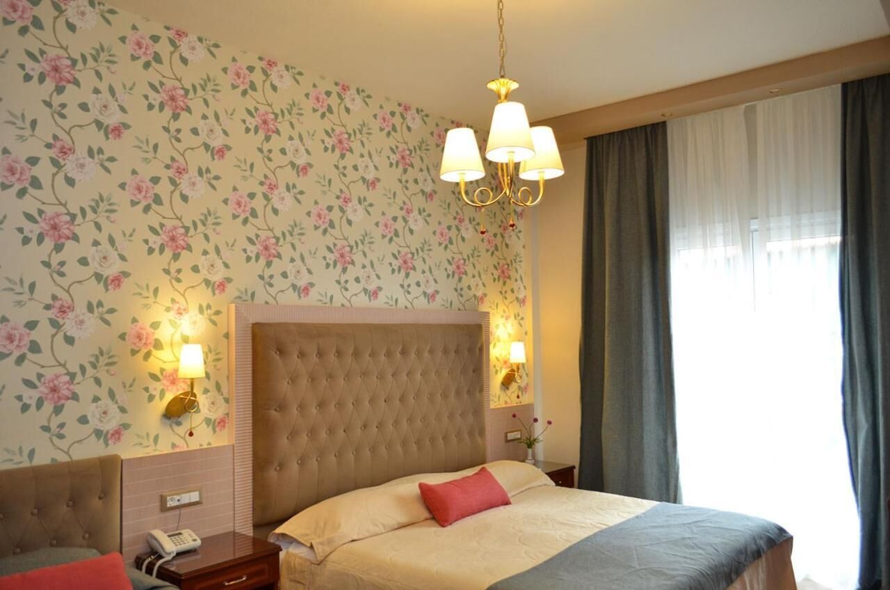 Una habitación de hotel con cabecera capitonada, papel tapiz floral, una araña y una lámpara de noche.