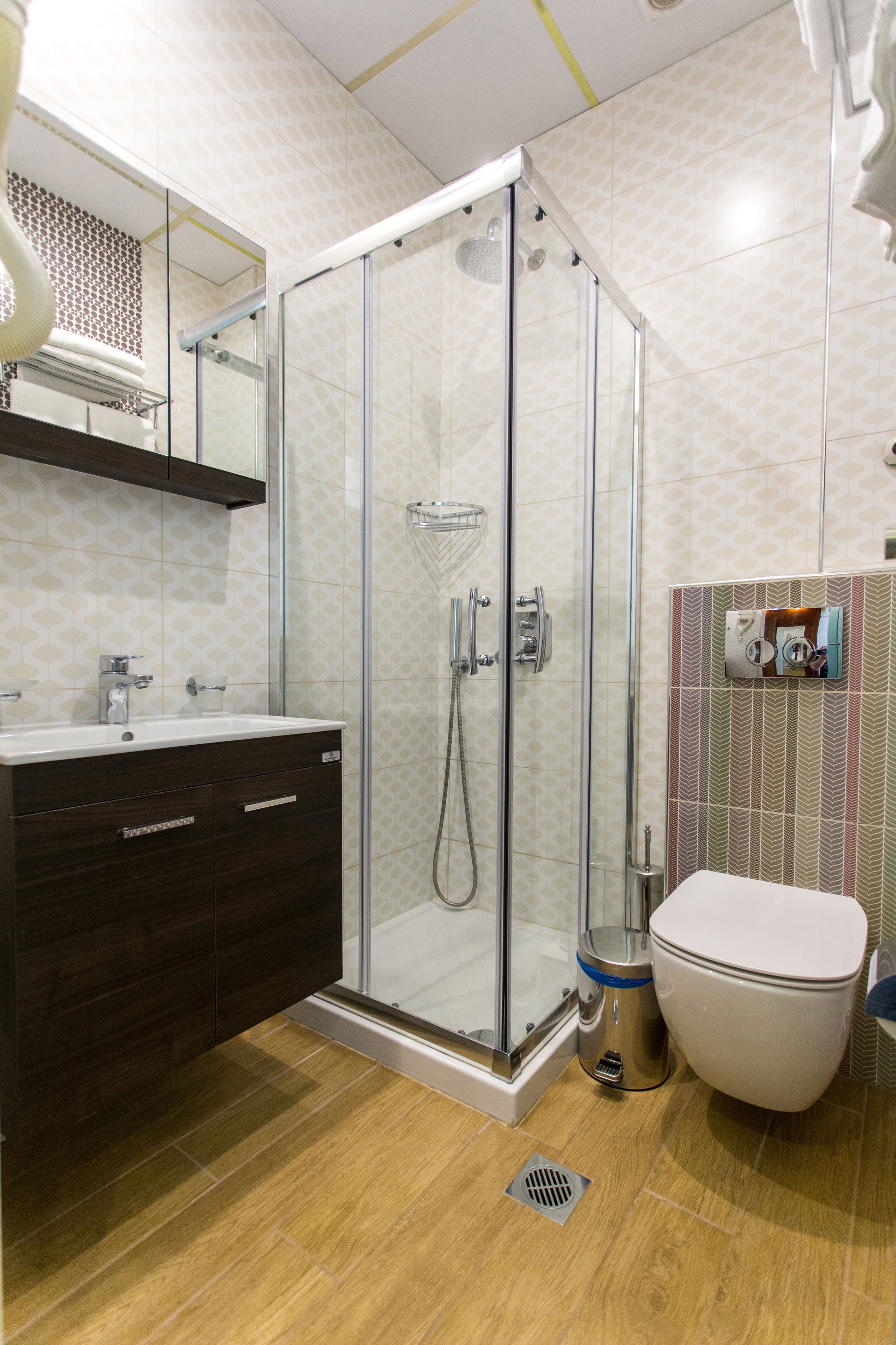 Un baño moderno con ducha de vidrio, tocador de madera oscura y un inodoro blanco.