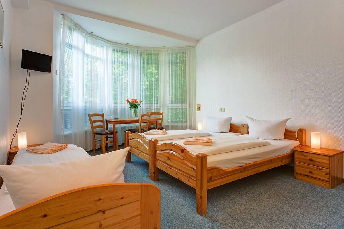A bedroom with two wooden beds, a desk, chairs, a TV, and a window with curtains.