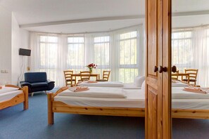 Una habitación con dos camas de madera, un escritorio, sillas y una televisión.