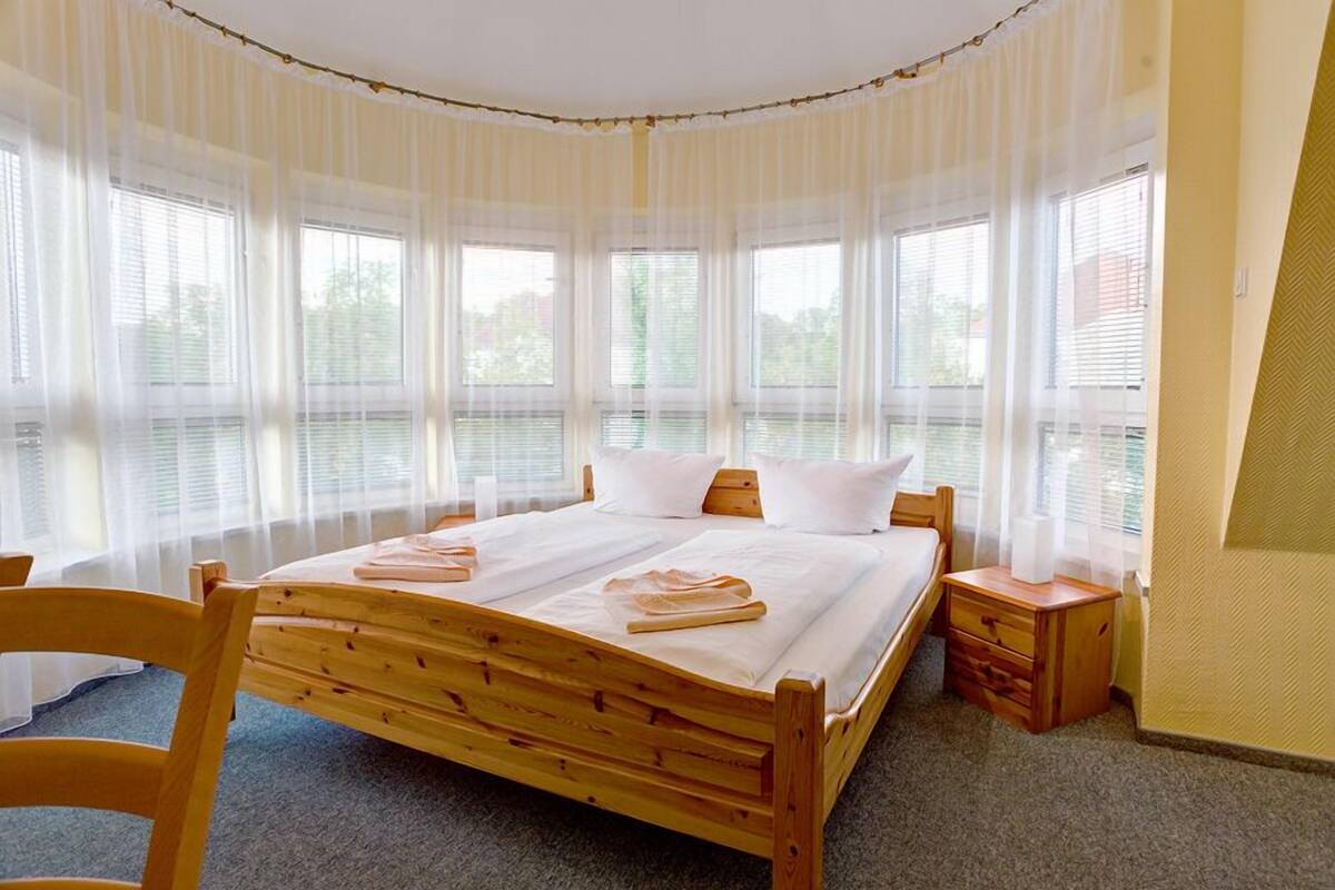 A bedroom with a wooden bed, white bedding, a wooden nightstand, and a chair.