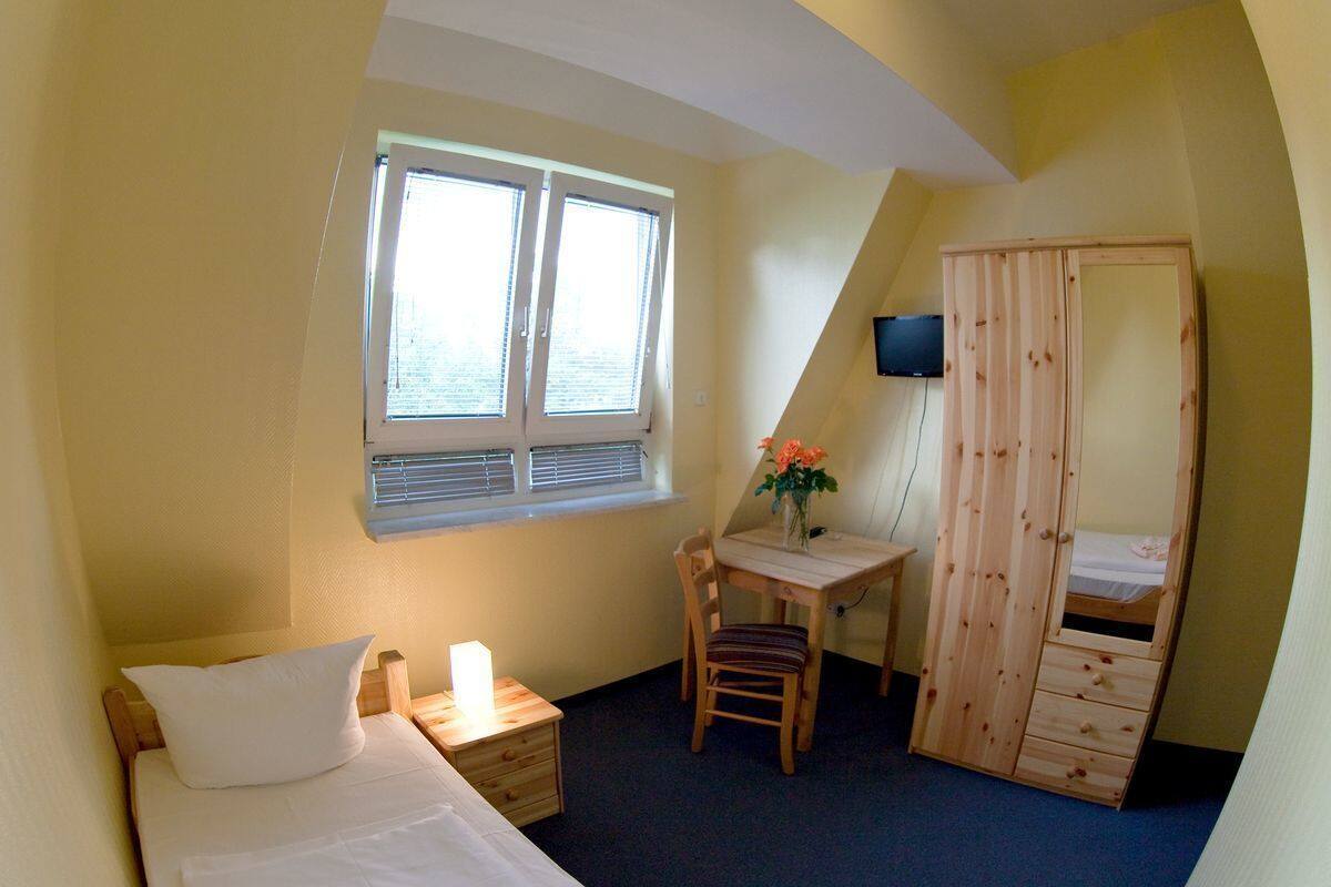 A bedroom with a bed, a desk, a chair, a wardrobe, and a window.
