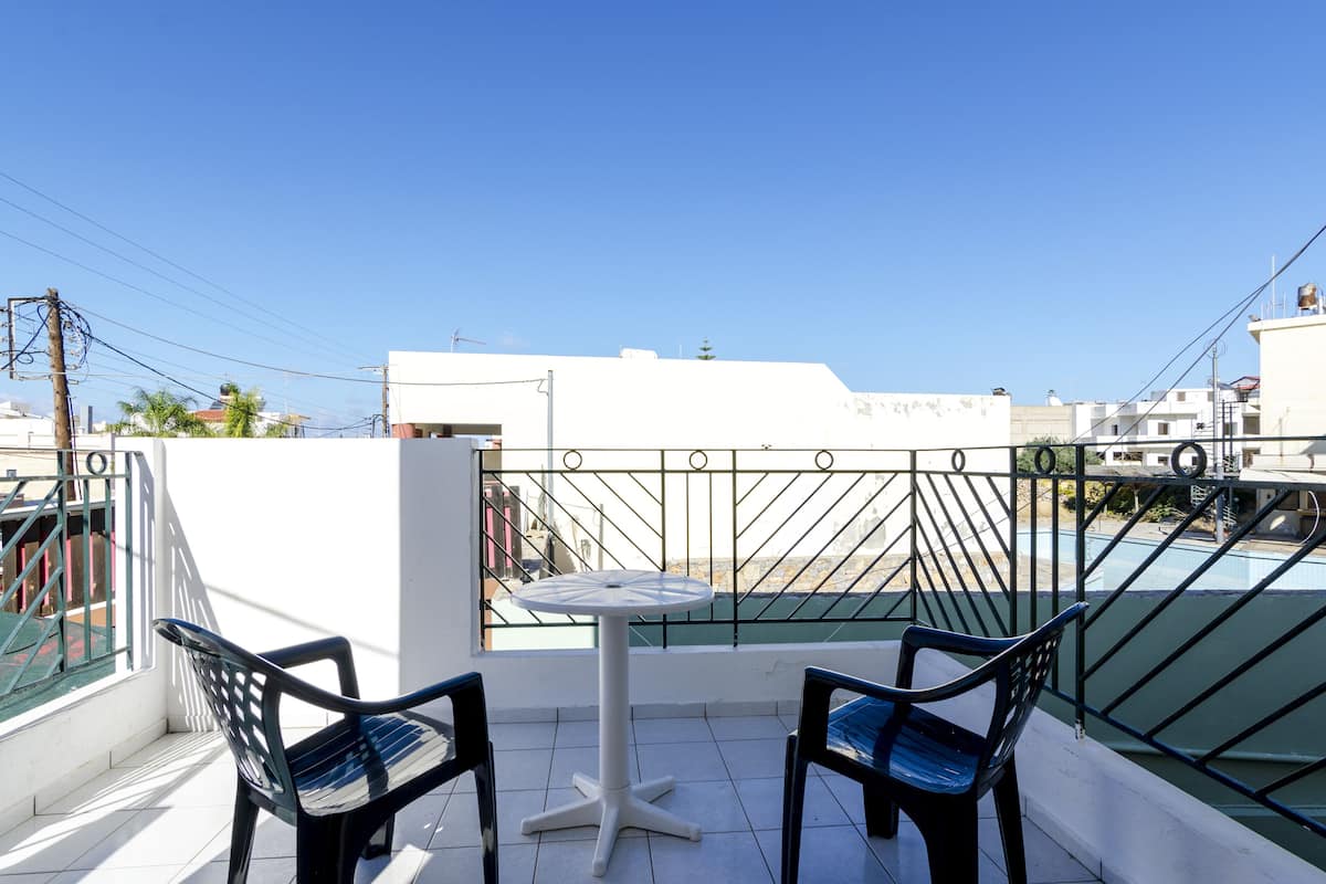 A balcony with two chairs and a small table, overlooking a swimming pool and buildings.