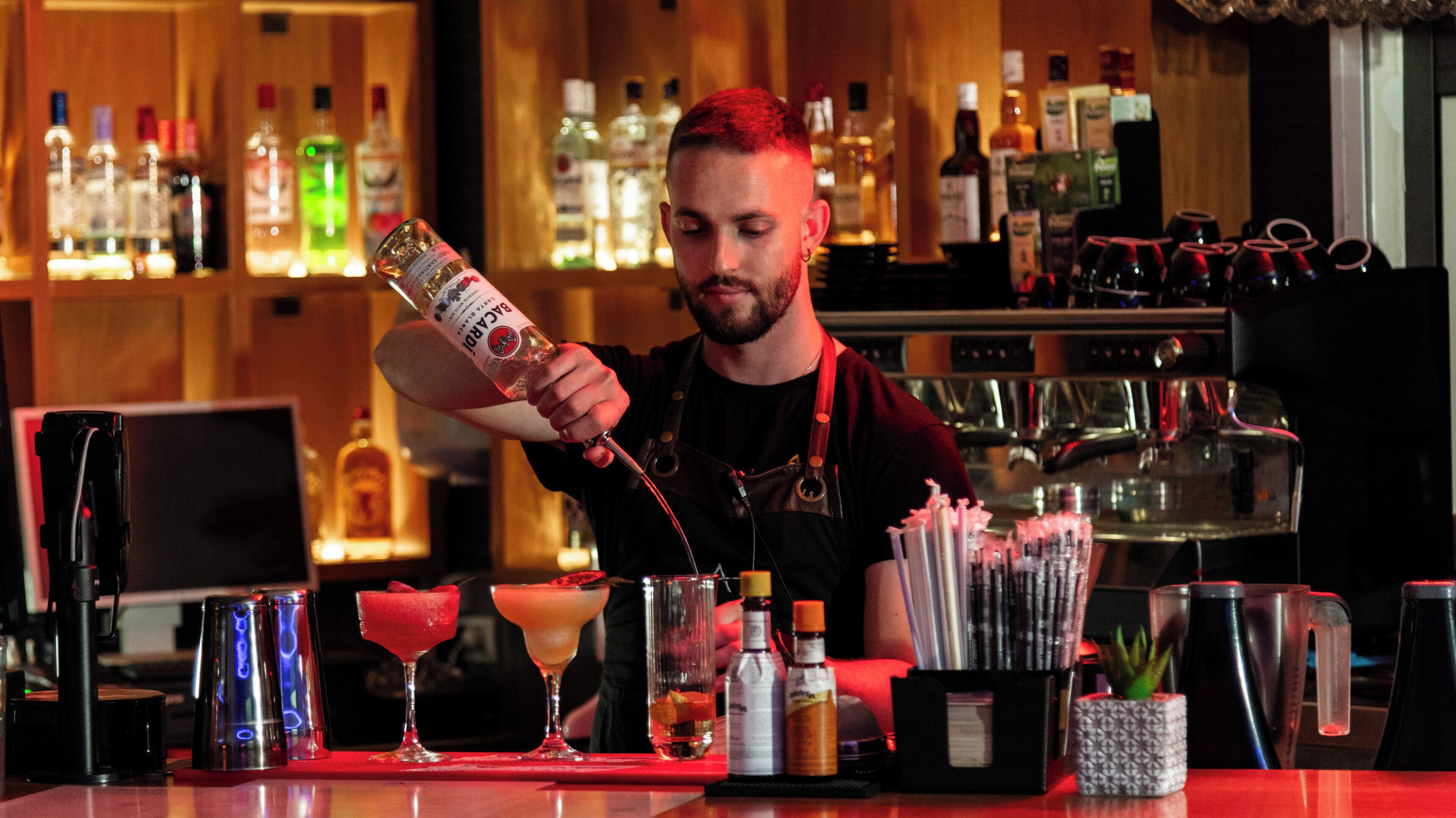 A bartender preparing a drink at a bar with various bottles and glasses.