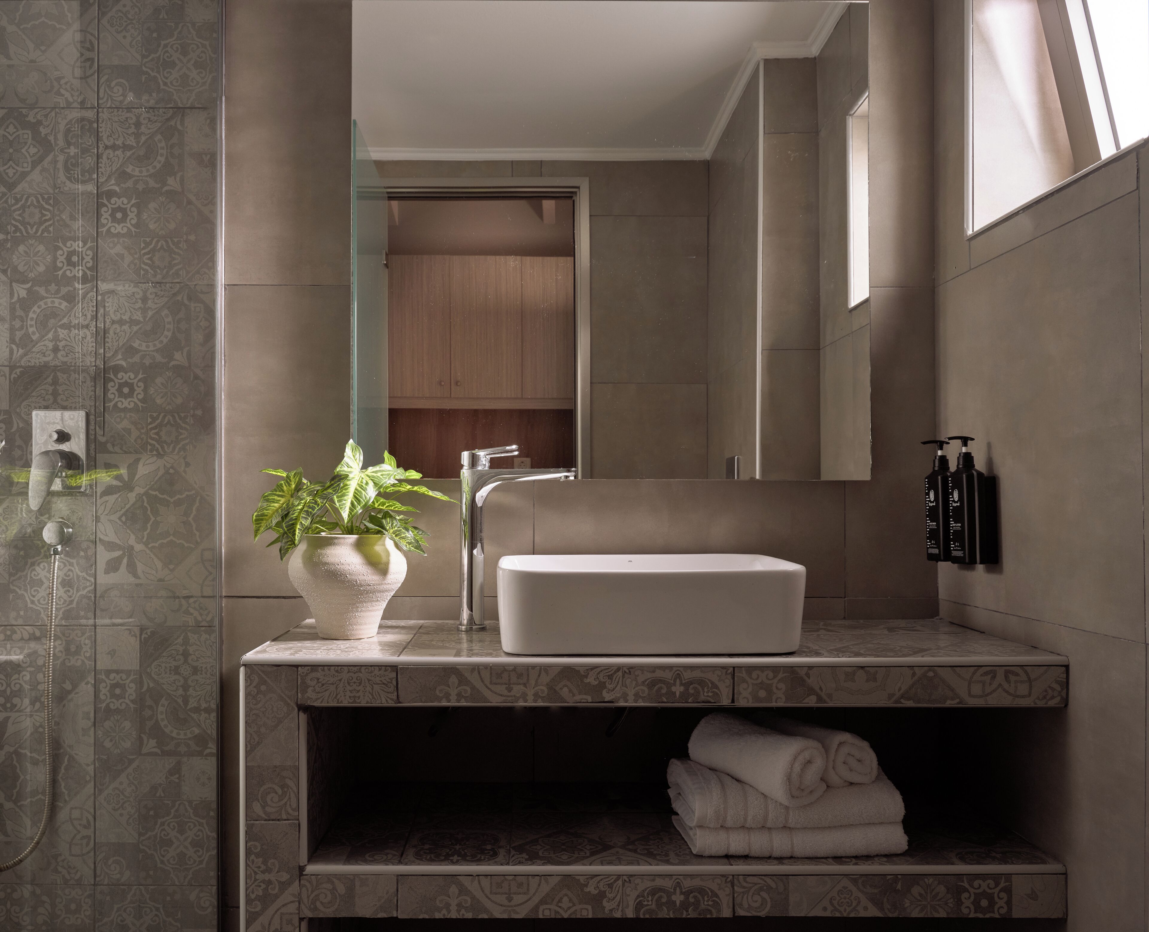 A modern bathroom with a white sink, a glass shower enclosure, a potted plant, and a towel shelf.