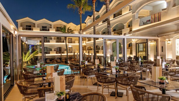 A multi-level hotel with a pool area, wicker furniture, and glass-enclosed balconies. - Atlantis Hotel (Zakynthos)