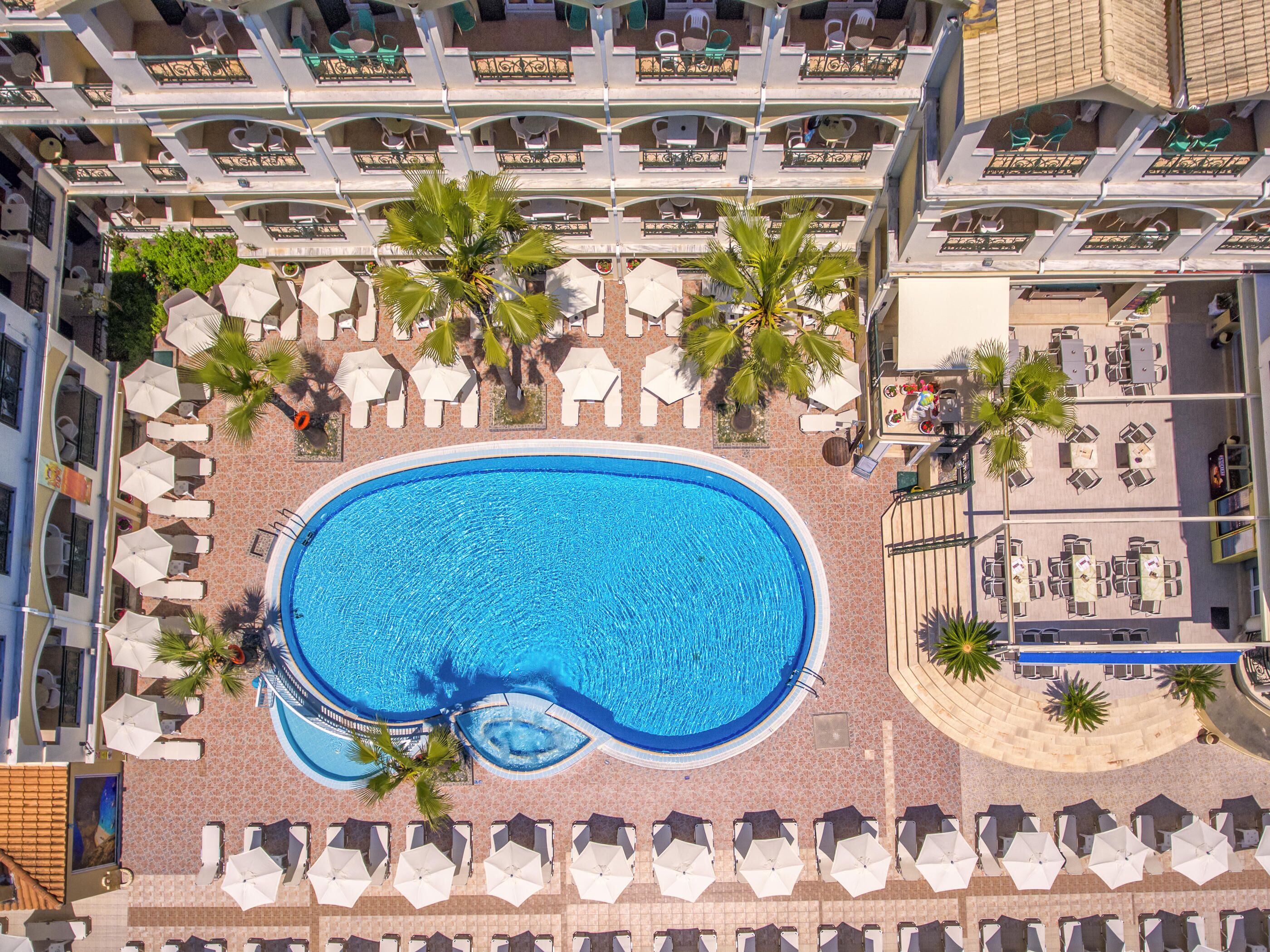 Vista aérea de un hotel con piscina central rodeada de tumbonas y palmeras.