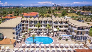 Un hotel con piscina central rodeada de tumbonas y sombrillas, varios balcones y vistas del paisaje circundante.