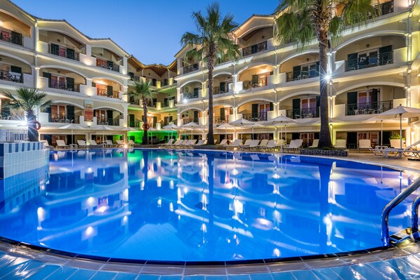 Un hotel de varios pisos con piscina, balcones y zonas de estar al aire libre.