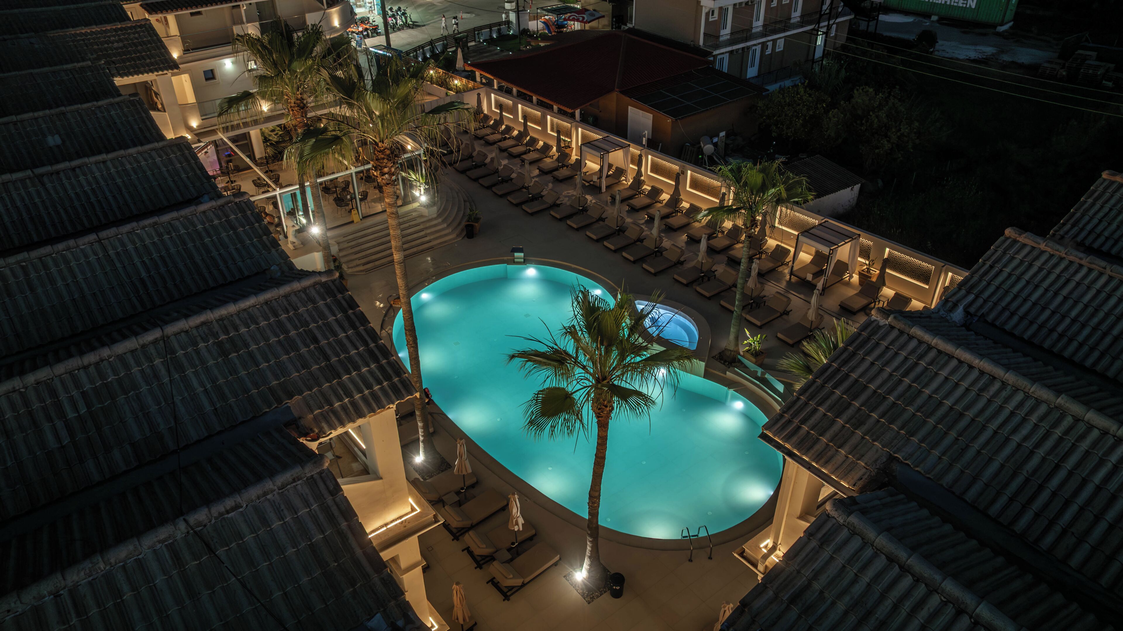 Una piscina en la azotea con sillones de descanso y palmeras.