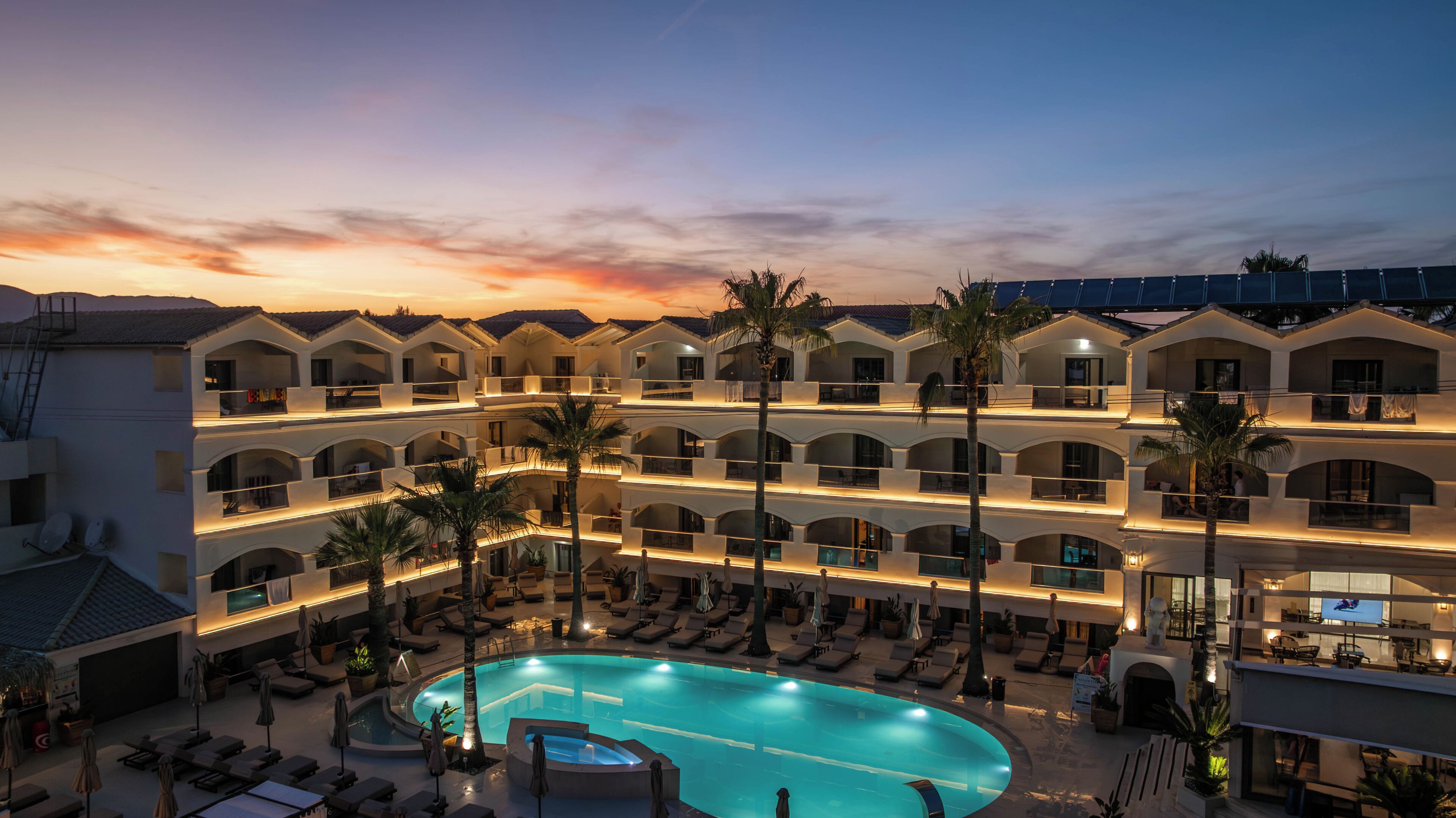 Un hotel de varios pisos con piscina, balcones y palmeras.