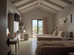 Habitación de hotel con una cama grande, un escritorio con silla, televisor montado en la pared y un balcón con vistas a la ciudad.