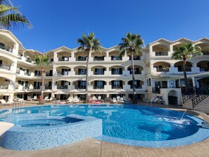 Un hotel con piscina, varios balcones y palmeras.