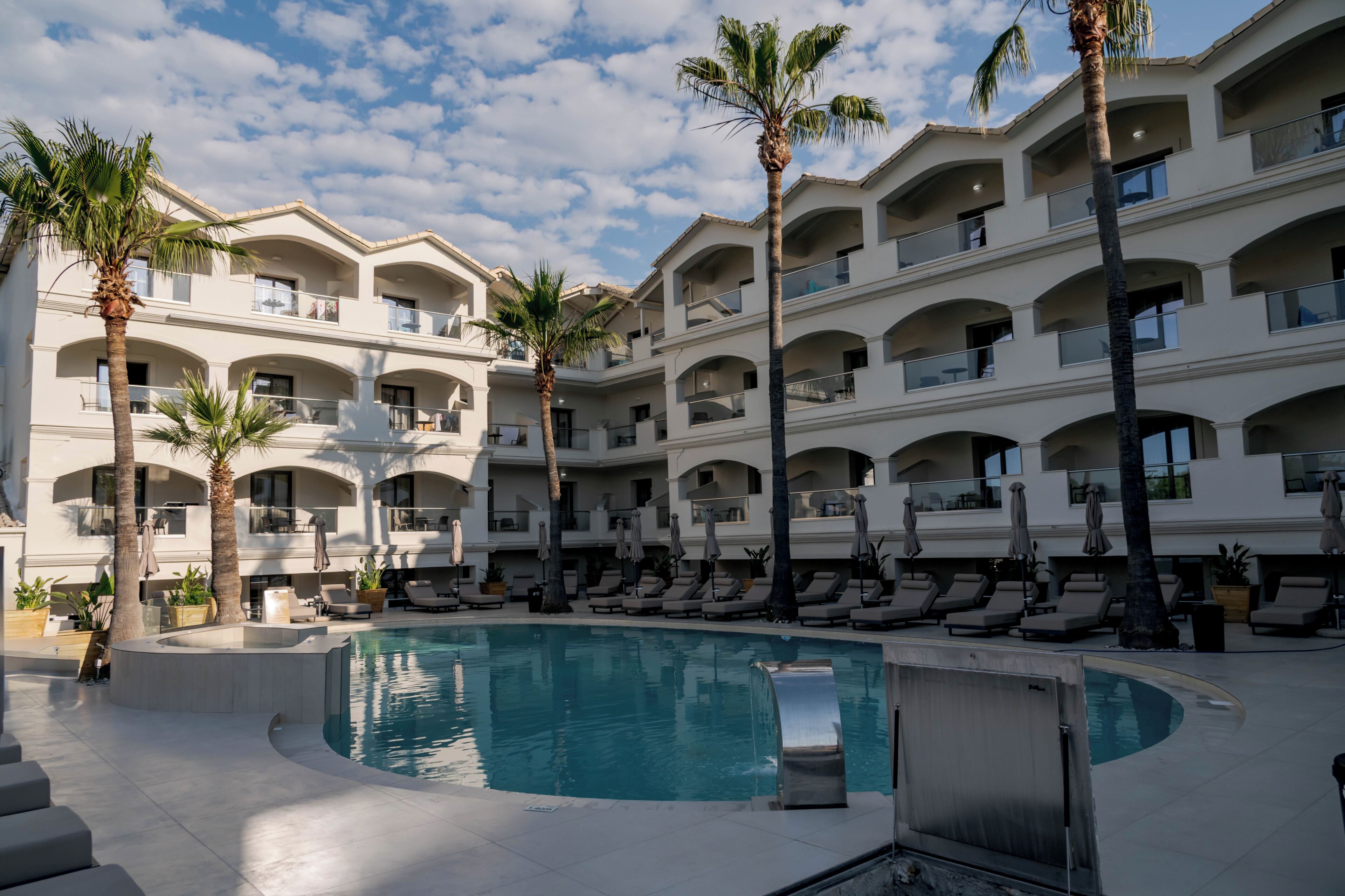 A hotel with a pool, palm trees, and multiple balconies.